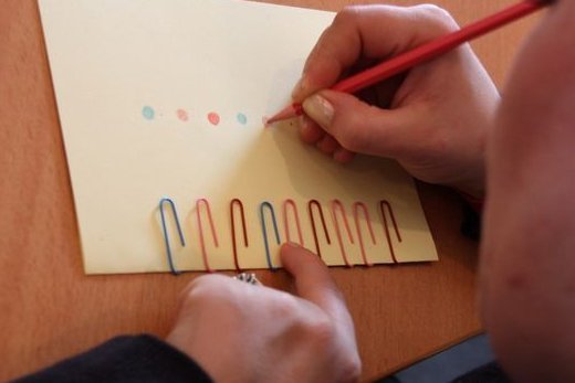  A child draws colorful dots over colorful paper clips in a row on an envelope.