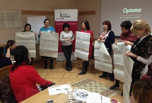 Damen präsentieren Flipchart-Bögen in einem Halbkreis um ihr Publikum.